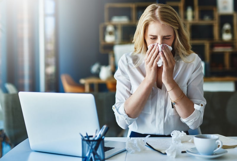 woman sneezing at desk