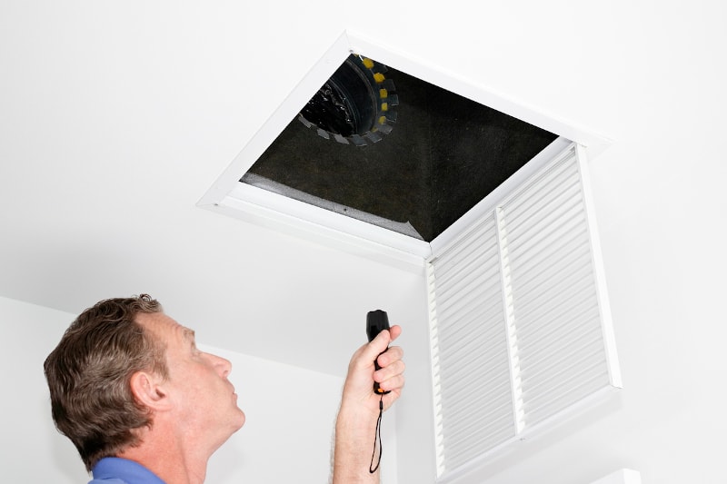 Man Looking At Ceiling Ducts With Flashlight